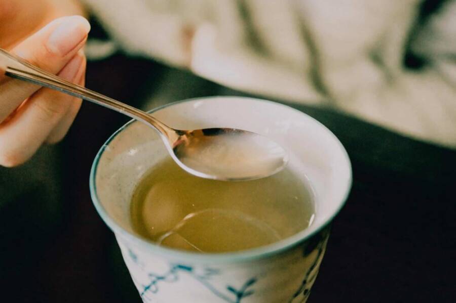 A hand holds a spoon over a cup of traditional Japanese green tea, offering a warm and soothing moment.