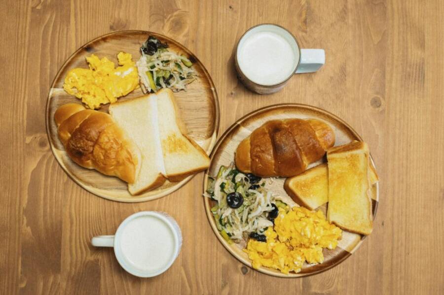 Delicious Japanese breakfast featuring eggs, toast, and milk on a wooden table setting.