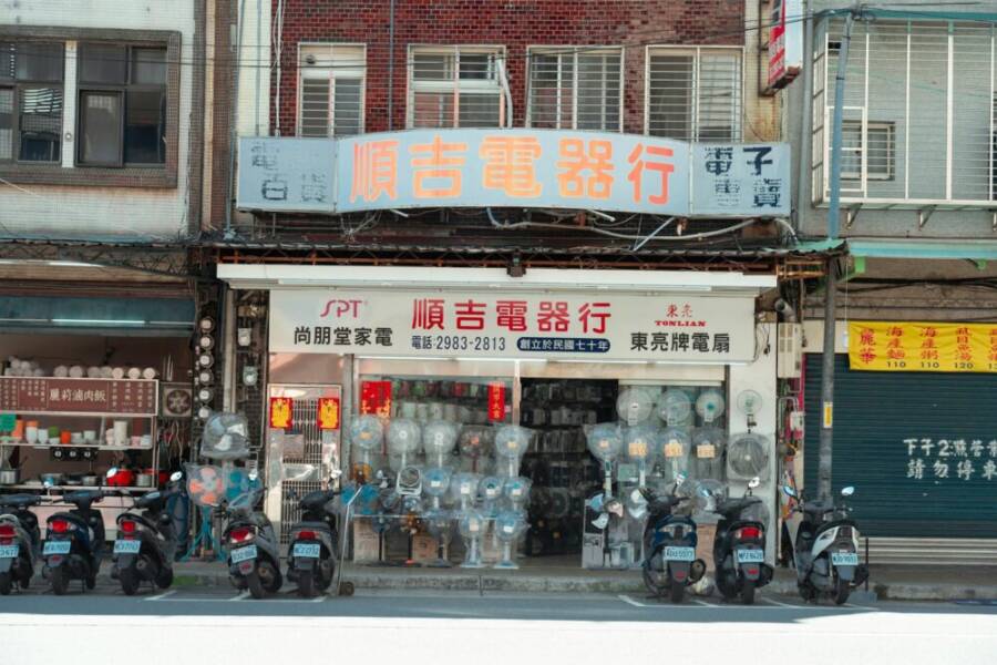 Vintage Taipei storefront with electronics display and parked scooters, showcasing urban culture.
