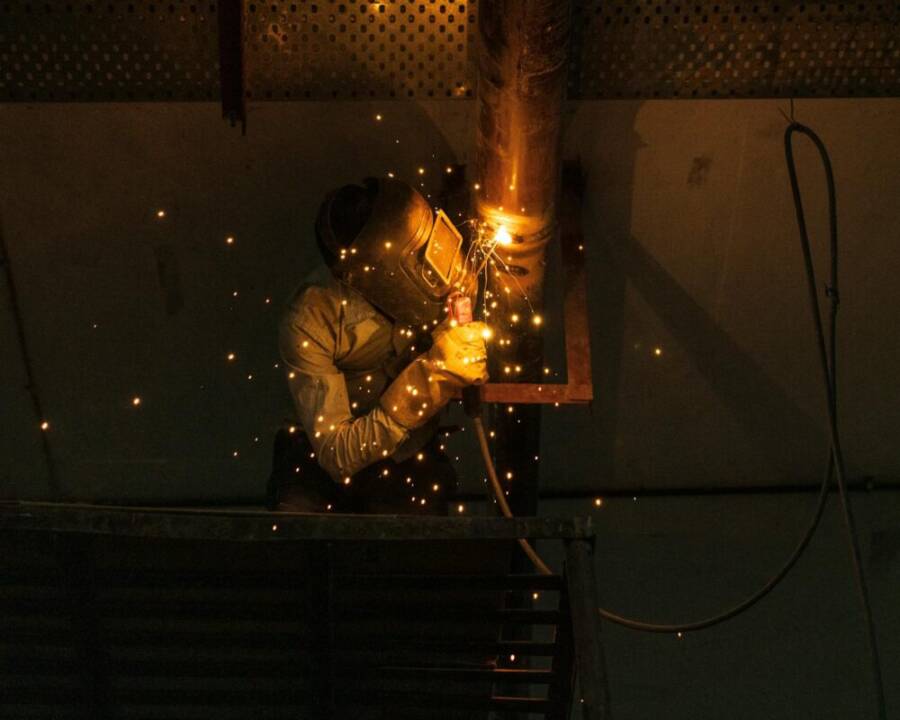 A welder at work indoors, creating bright sparks while welding metal pipes.