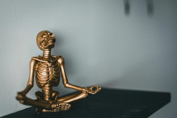 A golden skeleton statue sits in a meditative pose on a black surface against a neutral background.
