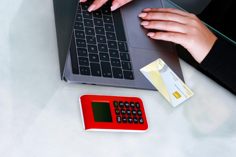 Hands using laptop with credit card and security device for online payment, emphasizing cybersecurity.