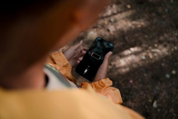 手機耗電元兇藏不住:電池使用狀況分析實用教學 Teenage boy holds a smartphone displaying low battery outdoors in a forest.