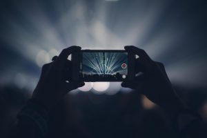 Hands holding smartphone to record concert with vibrant stage lights.