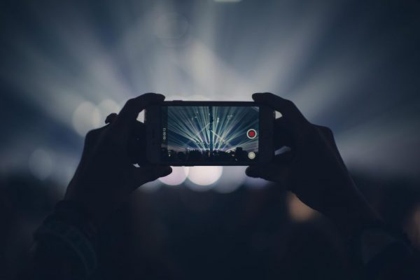 手機錄影畫面偏暗與閃爍:頻率與快門設定指南(含台灣60Hz) Hands holding smartphone to record concert with vibrant stage lights.