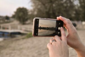 Close-up of hands using smartphone to capture a serene lake sunset view.