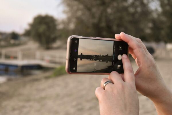 手機 AI 場景辨識功能:好用嗎?優化拍照的實用指南 Close-up of hands using smartphone to capture a serene lake sunset view.