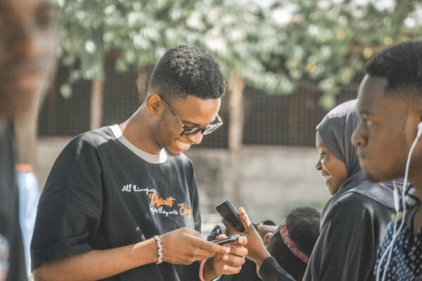 Group of young adults enjoying social interaction with mobile phones outdoors in Tanzania.