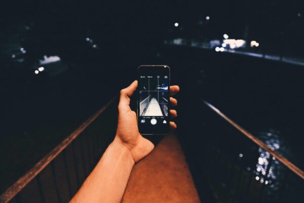 A close-up of a hand holding a smartphone taking a photo of a bridge at night.