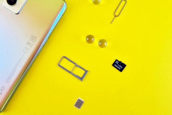 Close-up of a mobile phone with a SIM card, SIM tray, and memory card on a vibrant yellow surface.
