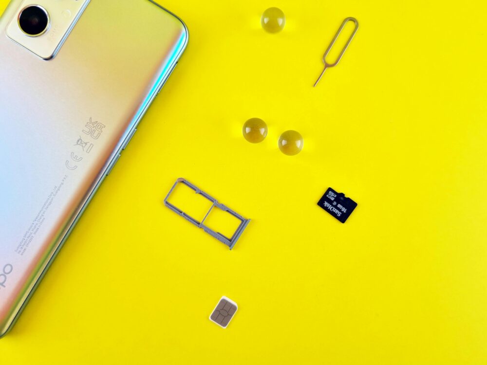 Close-up of a mobile phone with a SIM card, SIM tray, and memory card on a vibrant yellow surface