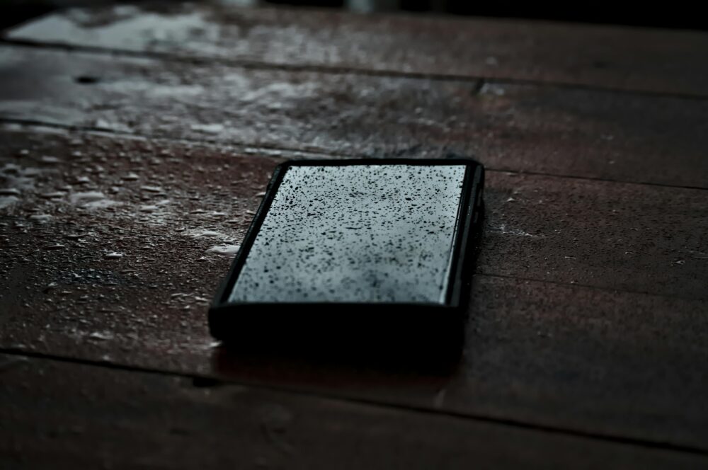 Close-up of a smartphone with droplets on a wet wooden surface, emphasizing waterproof technology