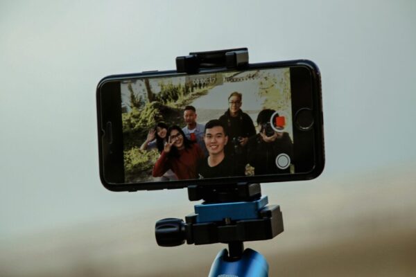 A group of friends enjoying video recording with a smartphone mounted on a tripod outdoors, capturing candid moments.