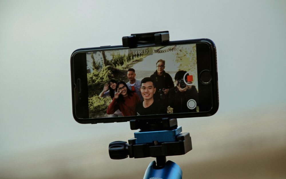A group of friends enjoying video recording with a smartphone mounted on a tripod outdoors, capturing candid moments.