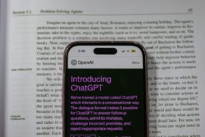 Smartphone showing OpenAI ChatGPT in focus, on top of an open book, highlighting technology and learning.