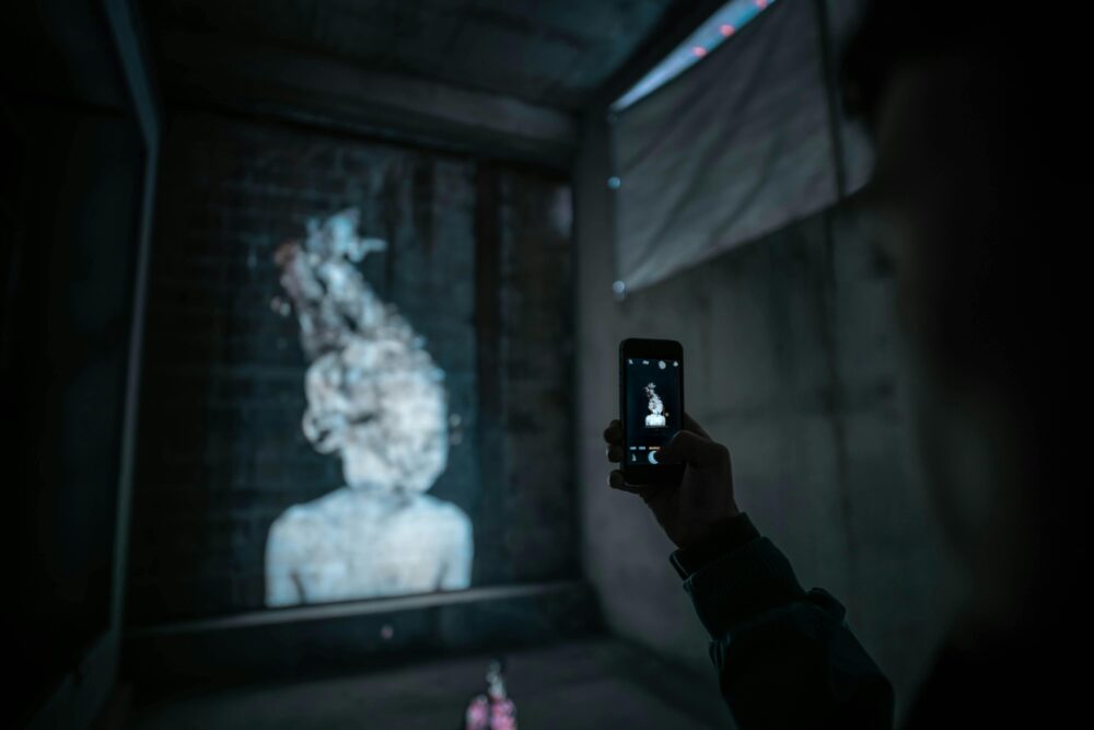 A person uses a smartphone to photograph urban artwork in low light conditions