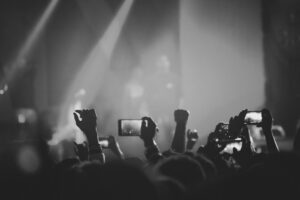 Black and white photo of a lively concert audience with raised hands and phones capturing the stage.