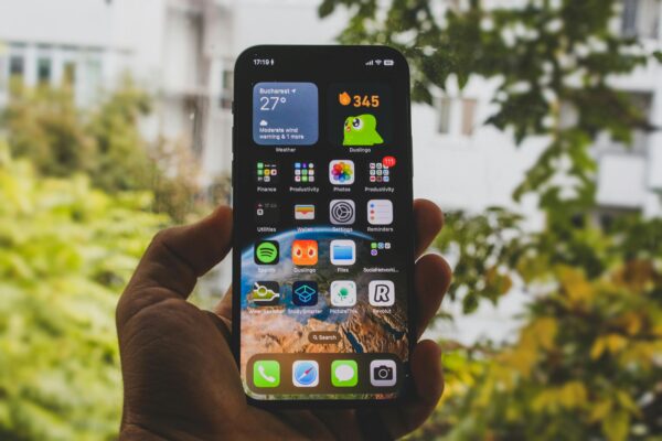 手機隱藏功能大集合:iOS與Android實用技巧全攻略(相機、電池、隱私、通訊) Close-up of a smartphone held outdoors in an autumn setting, showcasing apps and widgets.