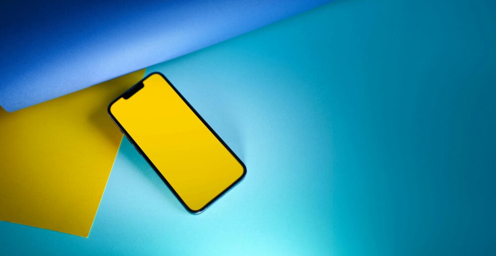 Stylish smartphone with a yellow screen on blue and yellow paper, ideal for tech and design concepts.
