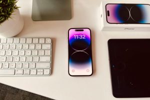 A sleek workspace setup featuring an iPhone with colorful display beside a keyboard and plant.
