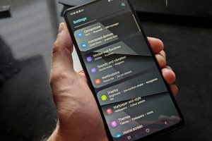 Hand holding smartphone displaying settings screen with various options evident.