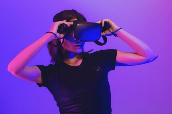 Apple Vision Pro 與 Meta Quest:XR 技術如何革新學習與娛樂 Woman wearing virtual reality headset immersed in a vibrant neon-lit gaming experience.