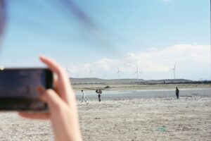 A smartphone captures people walking near wind turbines in a barren landscape.