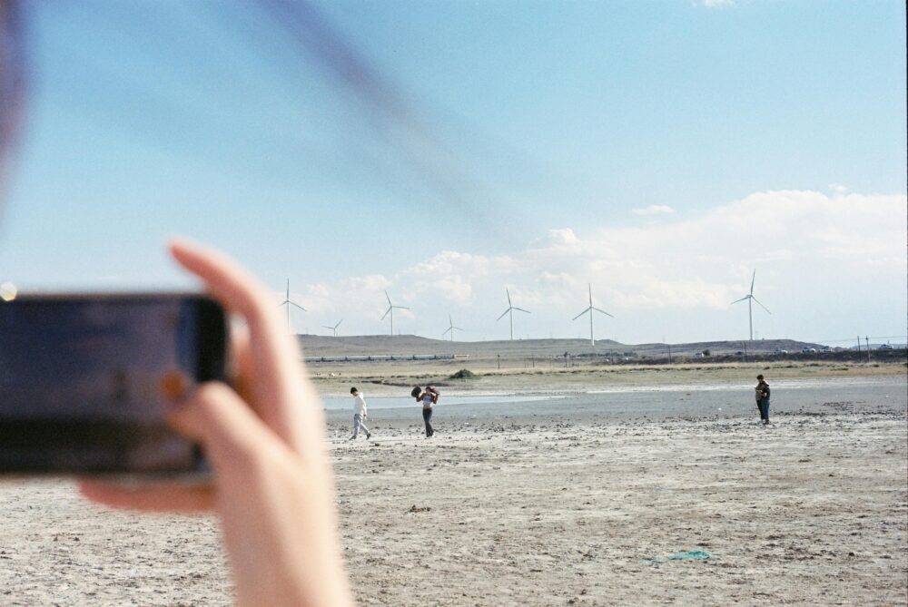 A smartphone captures people walking near wind turbines in a barren landscape.