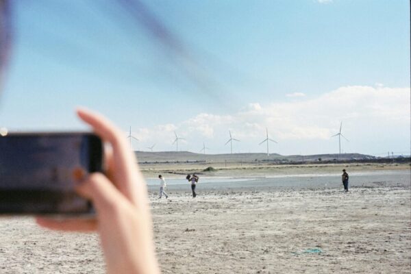 A smartphone captures people walking near wind turbines in a barren landscape.