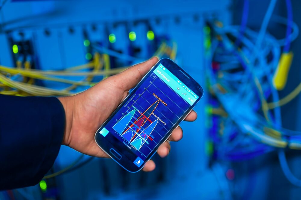 Hand holding smartphone displaying network analysis in high-tech server environment