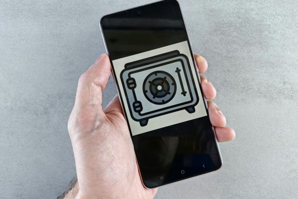 iPhone 與 Android 完整備份教學:本機與雲端全指南(今年最新) Close-up of a smartphone showing a safe icon held in a hand, symbolizing digital security.