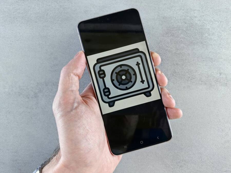 Close-up of a smartphone showing a safe icon held in a hand, symbolizing digital security.