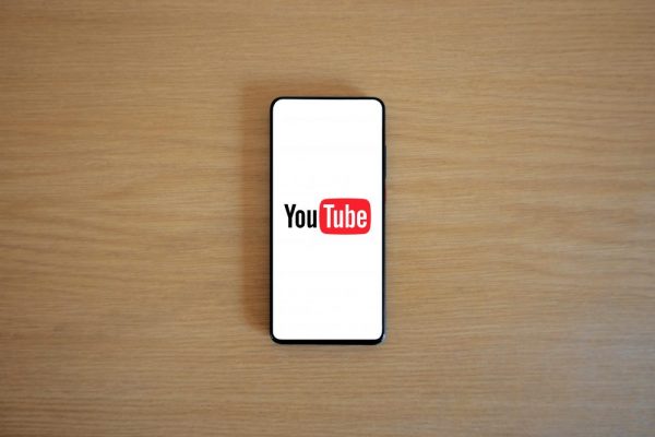 手機影音備份到 YouTube 與 Google Drive 的注意事項 Top view of smartphone displaying YouTube logo on a wooden surface, showcasing modern technology.