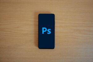 Top view of a smartphone showing Adobe Photoshop on a wooden surface.