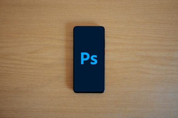 2025 年度手機攝影 APP 排行榜:AI 修圖、免費與付費精選(iPhone/Android) Top view of a smartphone showing Adobe Photoshop on a wooden surface.
