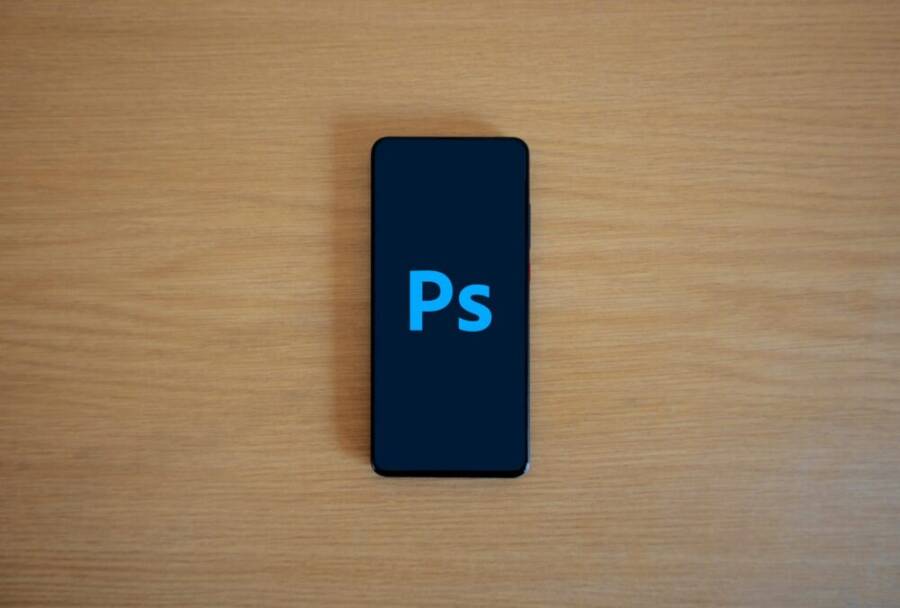 Top view of a smartphone showing Adobe Photoshop on a wooden surface.
