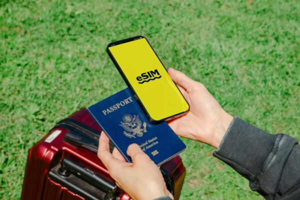Hands holding a smartphone with eSIM and a passport near a luggage outdoors, ideal for travel concepts