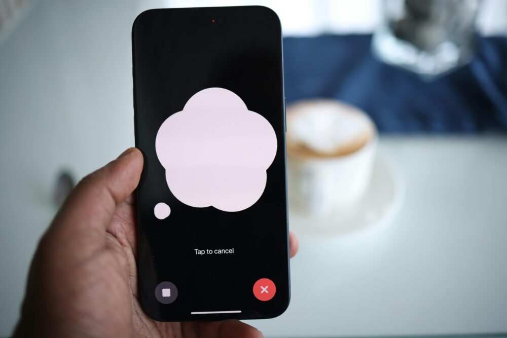 Close-up of a smartphone in hand with AI voice chat bubble and coffee in background
