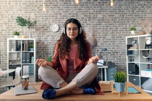 Young woman meditating with headphones in a modern office setting, practicing mindfulness.
