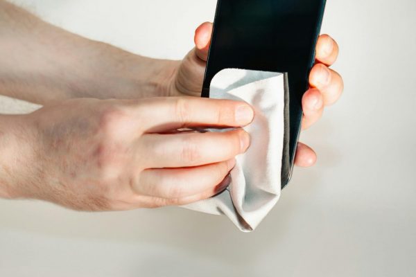 解決手機鍵盤延遲卡頓:震動、建議字與剪貼板優化指南 Hands cleaning smartphone screen with a soft cloth, emphasizing hygiene and device care.