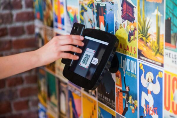 WhatsApp 多裝置登入與手機切換管理指南 A hand scanning a QR code with a smartphone on a wall covered in vibrant posters indoors.