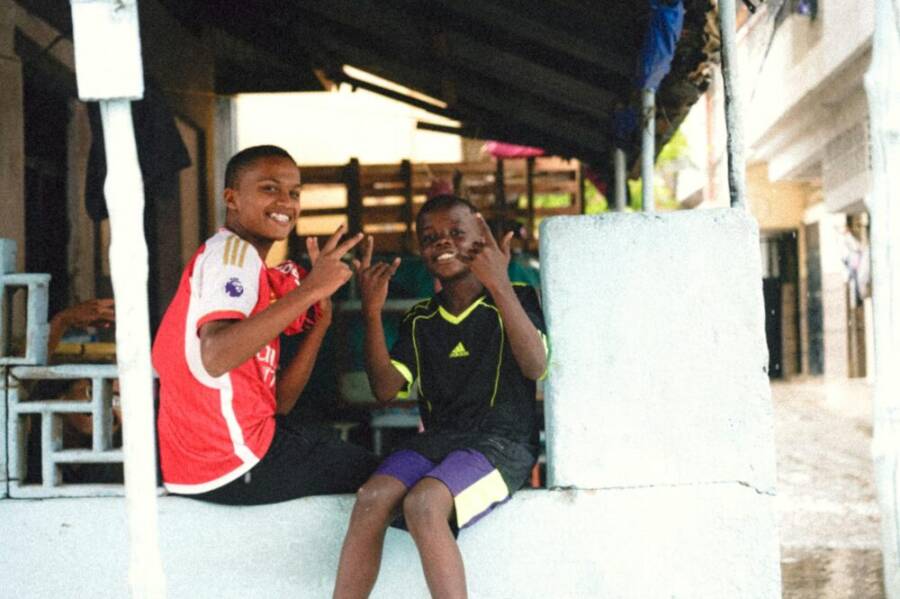 Two smiling children sitting outdoors, showing playful gestures, embodying friendship and fun.