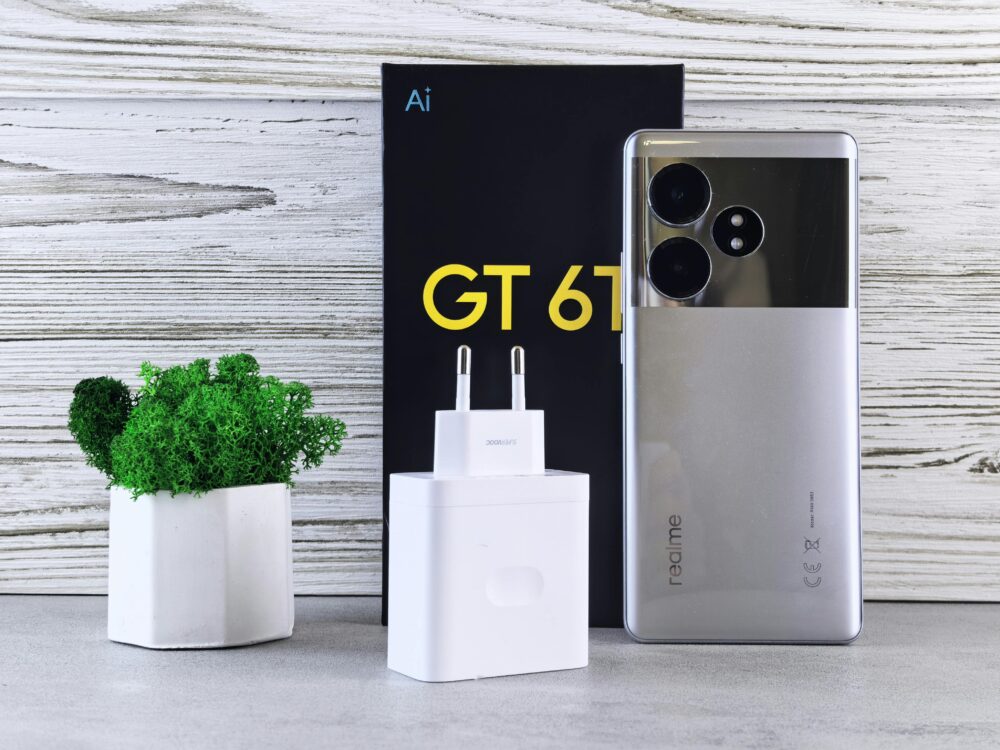 Close-up of a Realme smartphone with charger and potted plant on a wooden surface