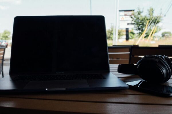 Laptop, headphones, smartphone on a wooden table outdoors, perfect for remote work setting.
