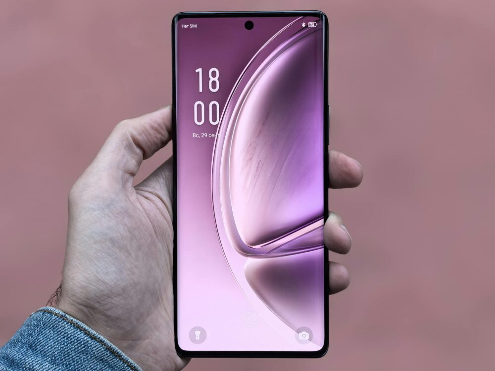 A person holding a sleek, modern smartphone with a purple screen against a plain background