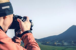 A woman photographer takes a photo of a scenic mountain landscape outdoors during the day.