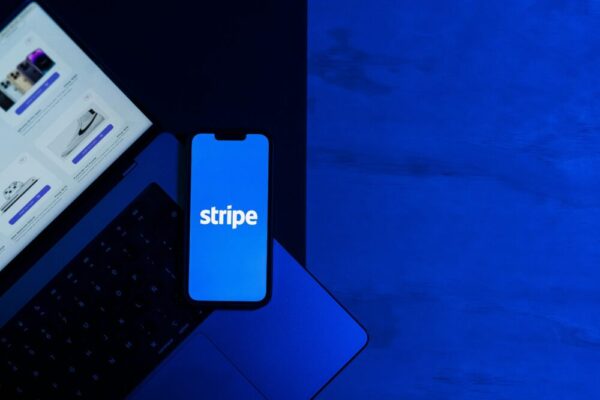 網路賺錢第一次收款指南:PayPal、Stripe、Wise 設定與稅務注意 A smartphone displaying the Stripe app placed on a laptop keyboard with a blue monochromatic tone.