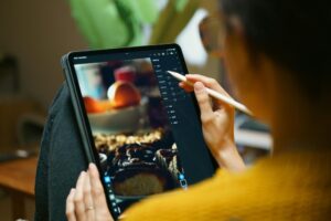 A woman uses a stylus to edit photos on a tablet, showcasing freelance creativity.