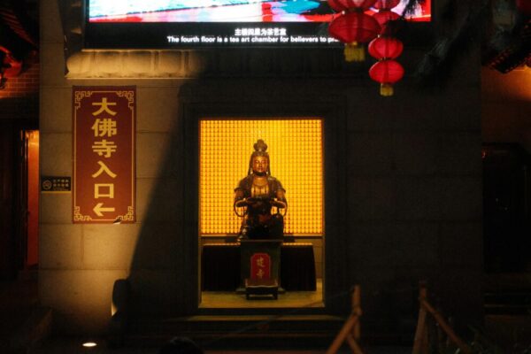 A Buddha statue illuminated at the entrance of a temple, surrounded by lanterns at night.
