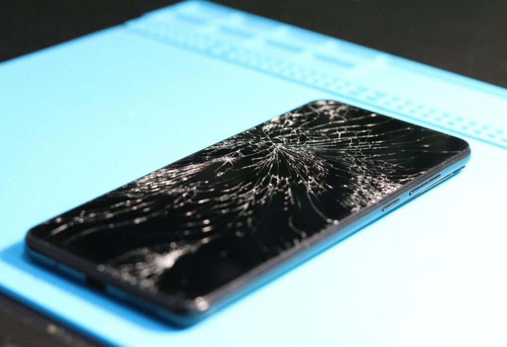 A cracked smartphone screen on a repair mat highlights technology mishaps.